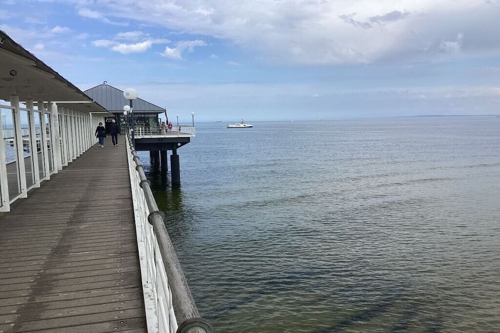 A pier extending into calm waters with a covered walkway and a building at the end.