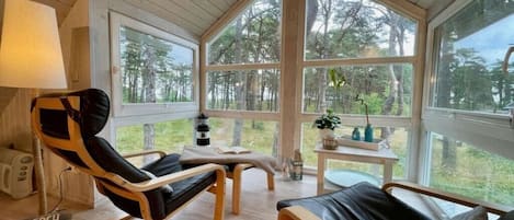 A cozy room with a large window, a chair, a small table, and a lamp.