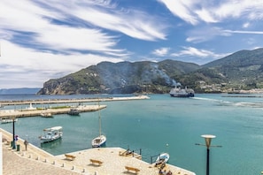 A coastal marina with boats, a large cruise ship, and a mountainous backdrop.