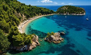 A coastal landscape with a beach, clear turquoise waters, and rocky outcrops.