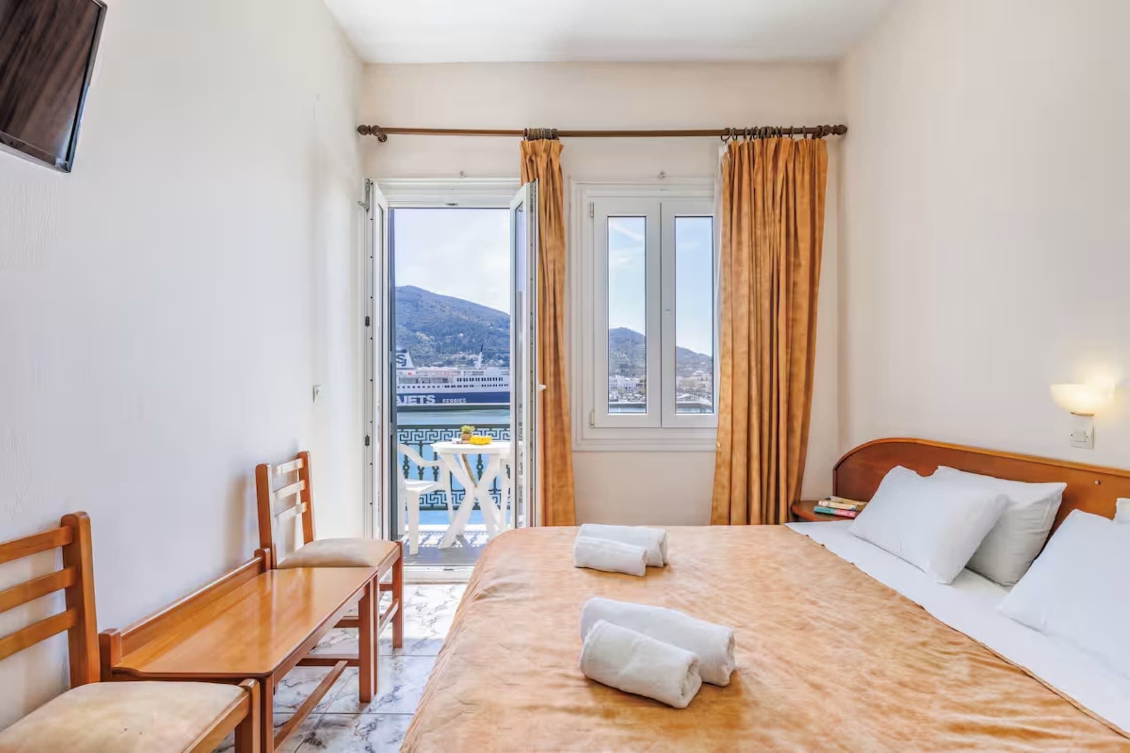 Ein Hotelzimmer mit einem Bett, einem Schreibtisch und einem Sessel. Es gibt ein Fenster mit Vorhängen und Blick auf eine Stadtlandschaft und Berge.