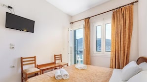 A hotel room with a bed, a desk, a chair, a TV mounted on the wall, and a window with curtains.