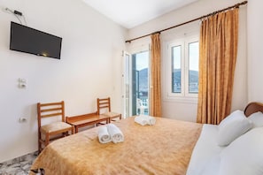A hotel room with a bed, a desk, a chair, a TV mounted on the wall, and a window with curtains.