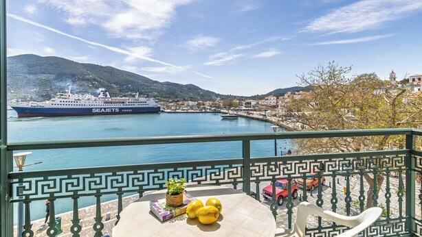 A balcony with a view of a ferry, a table with a book and lemons, and a green railing.