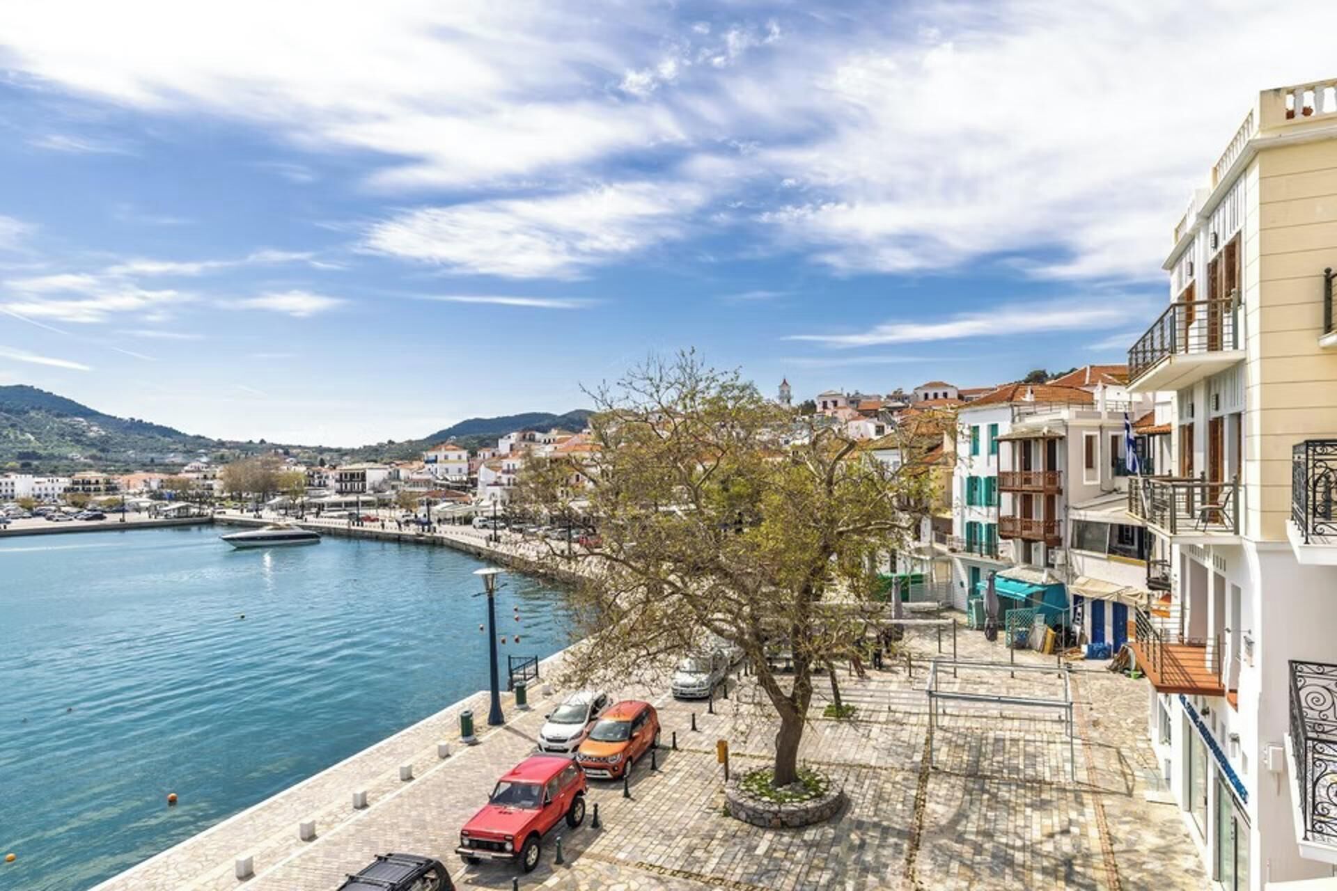 A coastal town with a marina, parked cars, and buildings along the waterfront.