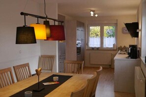 Ruokailutilassa on puinen pöytä ja tuolit, riippuvalaisin sekä avoimesta ovesta avautuva näkymä keittiöön.
