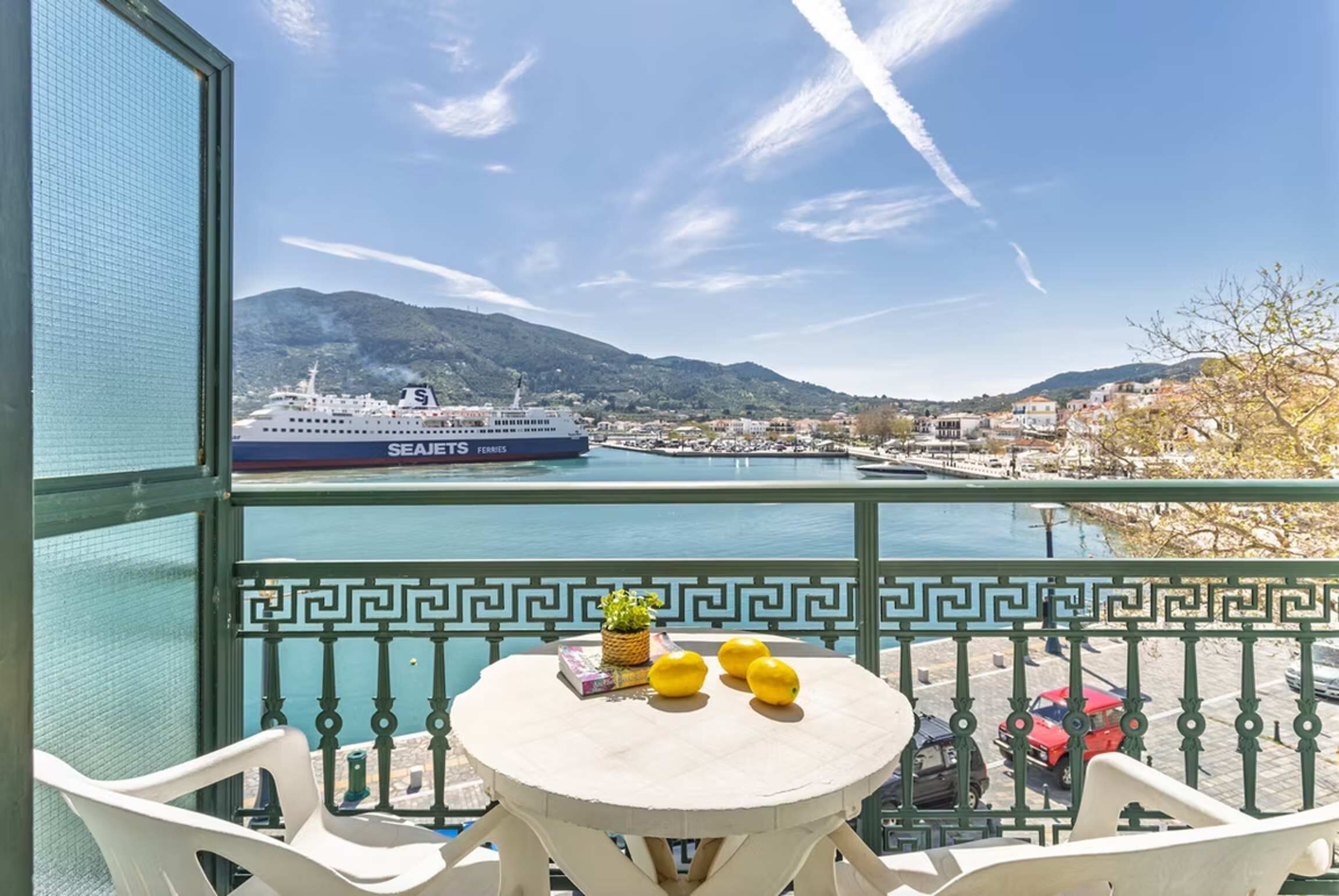 Un balcón con vista a un crucero, una mesa con objetos amarillos y una barandilla estampada.