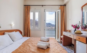 A hotel room with a bed, a desk, a chair, a mirror, and a view of the city and mountains through the window.
