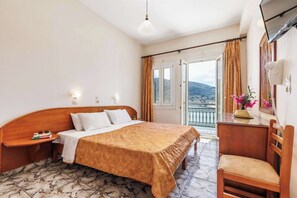 A hotel room with a bed, bedside table, lamp, chair, and a view of the city through the window.