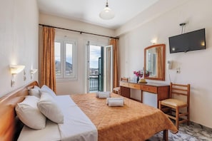 A hotel room with a bed, a desk, a chair, a TV, and a balcony with curtains.