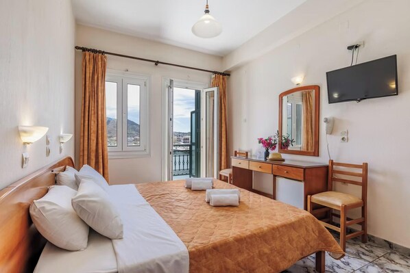 A hotel room with a bed, a desk, a chair, a TV, and a balcony with curtains.