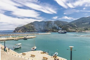 A coastal marina with boats, a large cruise ship, and a mountainous backdrop.