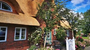 A brick house with a thatched roof, a garden with flowering plants, and a white gate. - "Pirates" in the Boatswain's House (Nebel)
