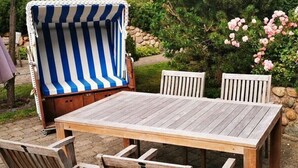 A wooden table with four chairs, a striped beach chair, and a garden with shrubs and flowers. - "Pirates" in the Boatswain's House (Nebel)
