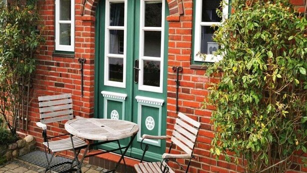 A brick building with green doors and windows, a round table, and two wooden chairs. - "Pirates" in the Boatswain's House (Nebel)