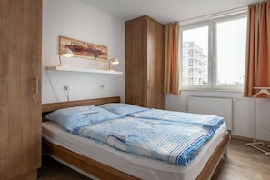 Una camera da letto con un letto, un'armadiatura in legno, una mensola con una lampada e una finestra con tende.