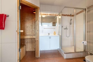 Un bagno con box doccia in vetro, un lavandino bianco e un armadietto in legno.