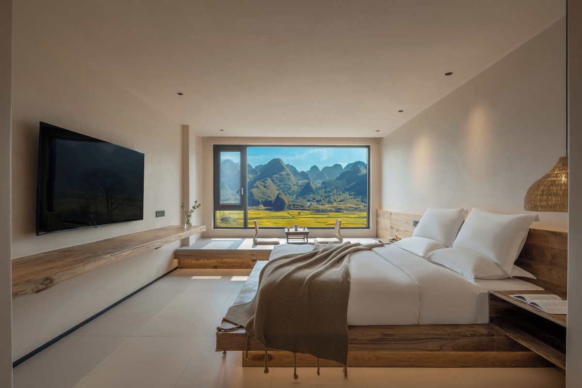 Un dormitorio moderno con una cama grande, un televisor de pantalla plana y vistas a las montañas a través de un amplio ventanal.