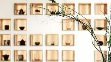 Una habitación con una mesa de madera, un juego de té, un cuadro enmarcado y una pared con estanterías que contienen varios objetos.