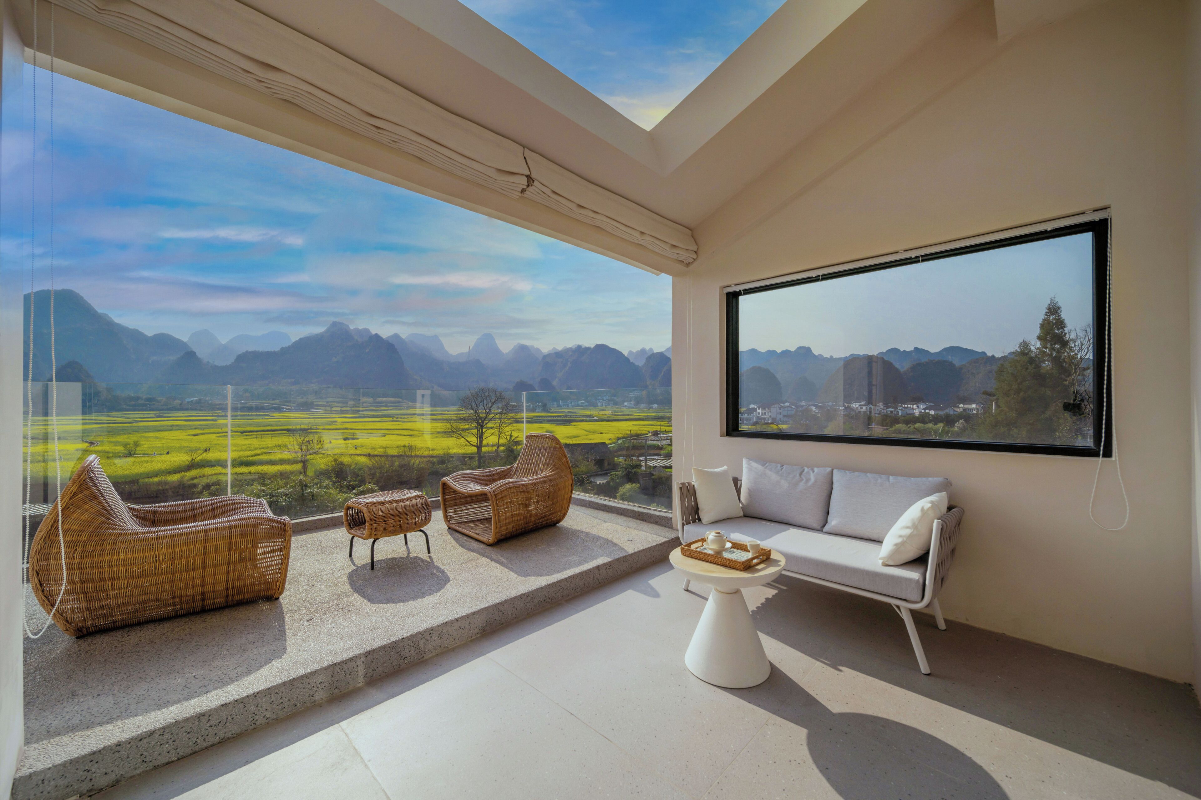 A modern balcony with a view of a mountainous landscape, furnished with wicker chairs and a white sofa.
