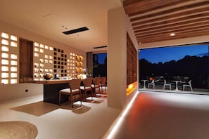 Un interior moderno con comedor, cocina con barra y un amplio ventanal con vistas a un paisaje montañoso.