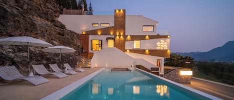 A modern house with a swimming pool, outdoor seating, and a view of the mountains.