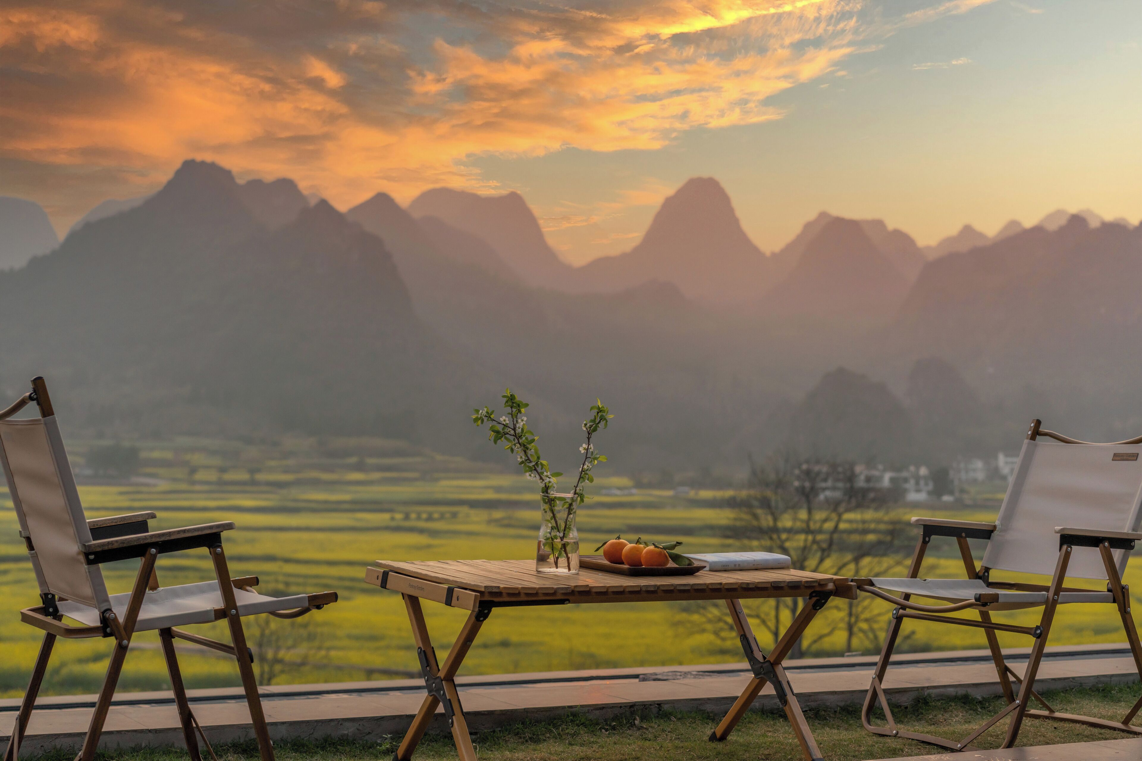 Une table ornée d’un vase de fleurs et de fruits, deux chaises, et une vue sur les montagnes.