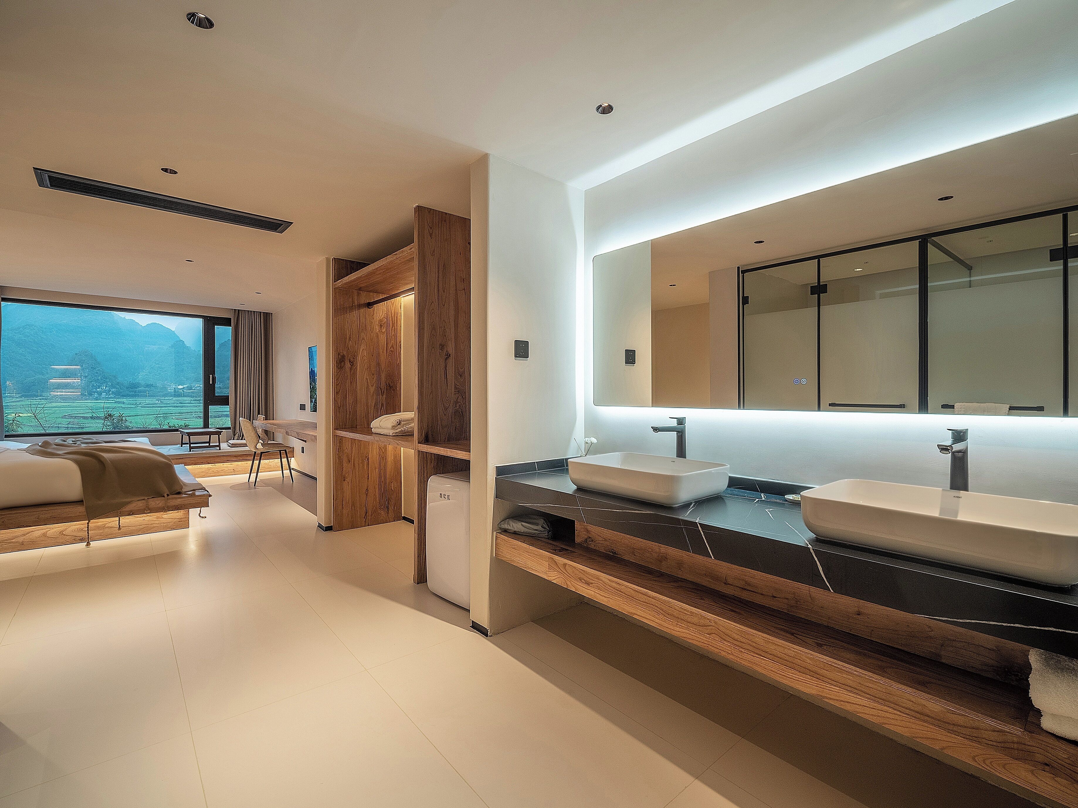 A modern bathroom with a large mirror, two sinks, and a view of a mountainous landscape.