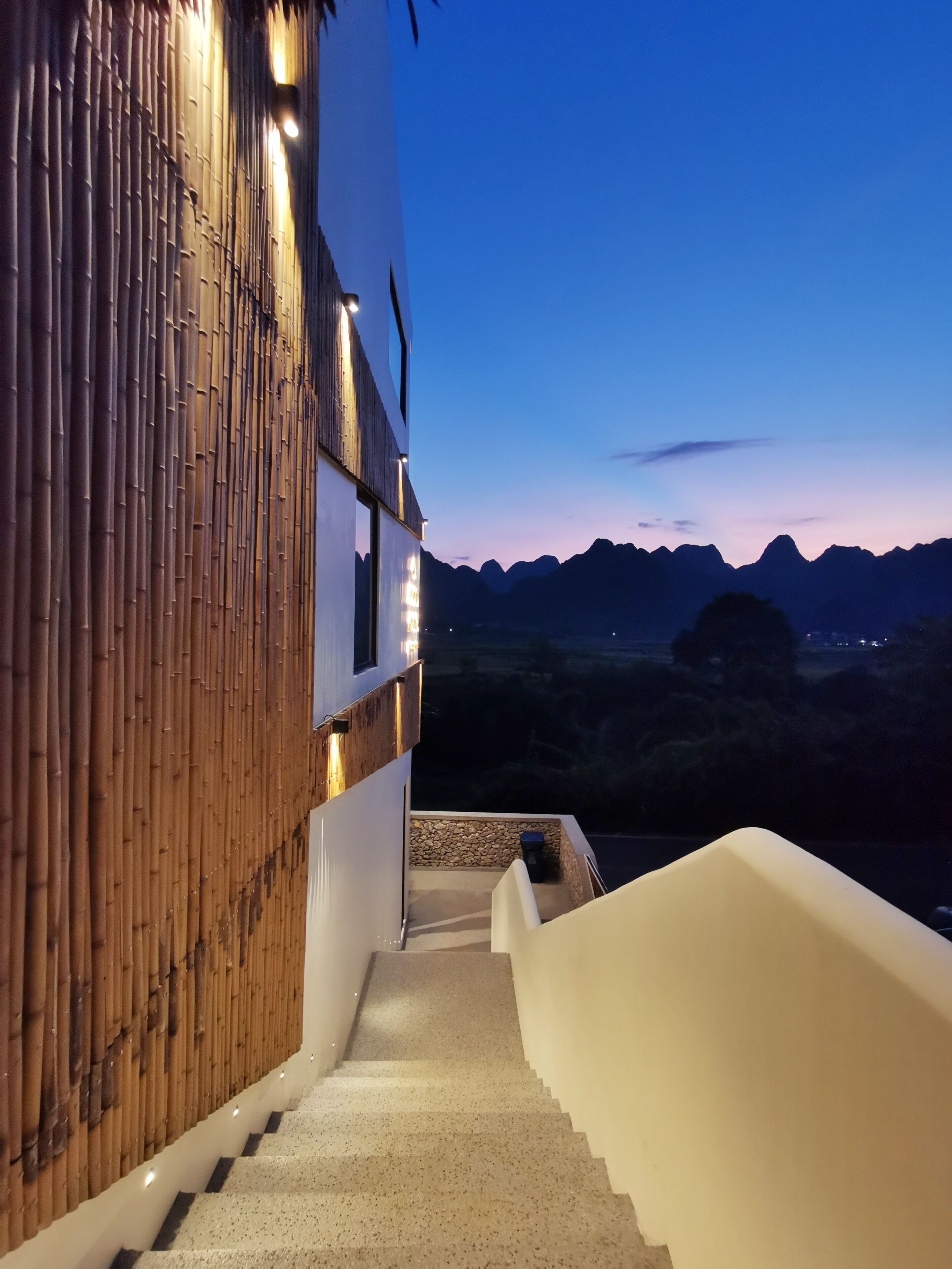 Un escalier menant à un bâtiment dont la façade extérieure est recouverte de bambou, avec une vue sur les montagnes en arrière-plan.