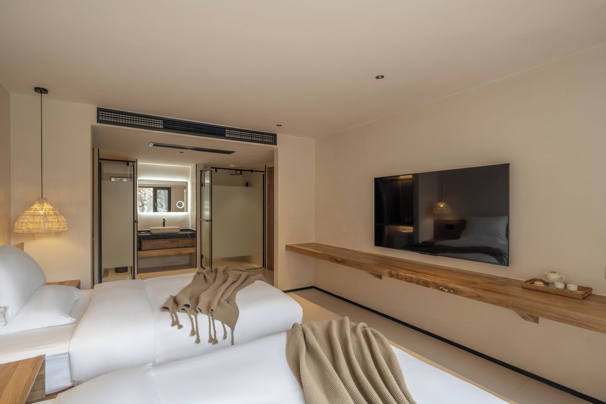 Habitación de hotel moderna con una cama, un televisor montado en la pared y un baño visible a través de una puerta abierta.