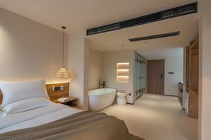 A modern hotel room with a large bed, a bedside table, a hanging light fixture, a bathtub, and a separate shower area.