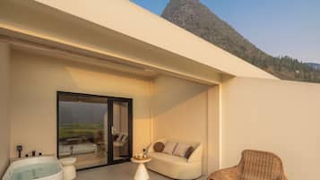 A modern outdoor living space with a glass door leading to a balcony, a white sofa, a wicker chair, and a hot tub.