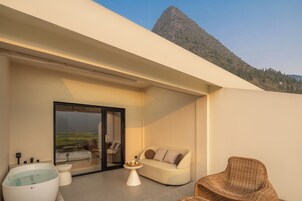 A modern outdoor living space with a glass door leading to a balcony, a white sofa, a wicker chair, and a hot tub.