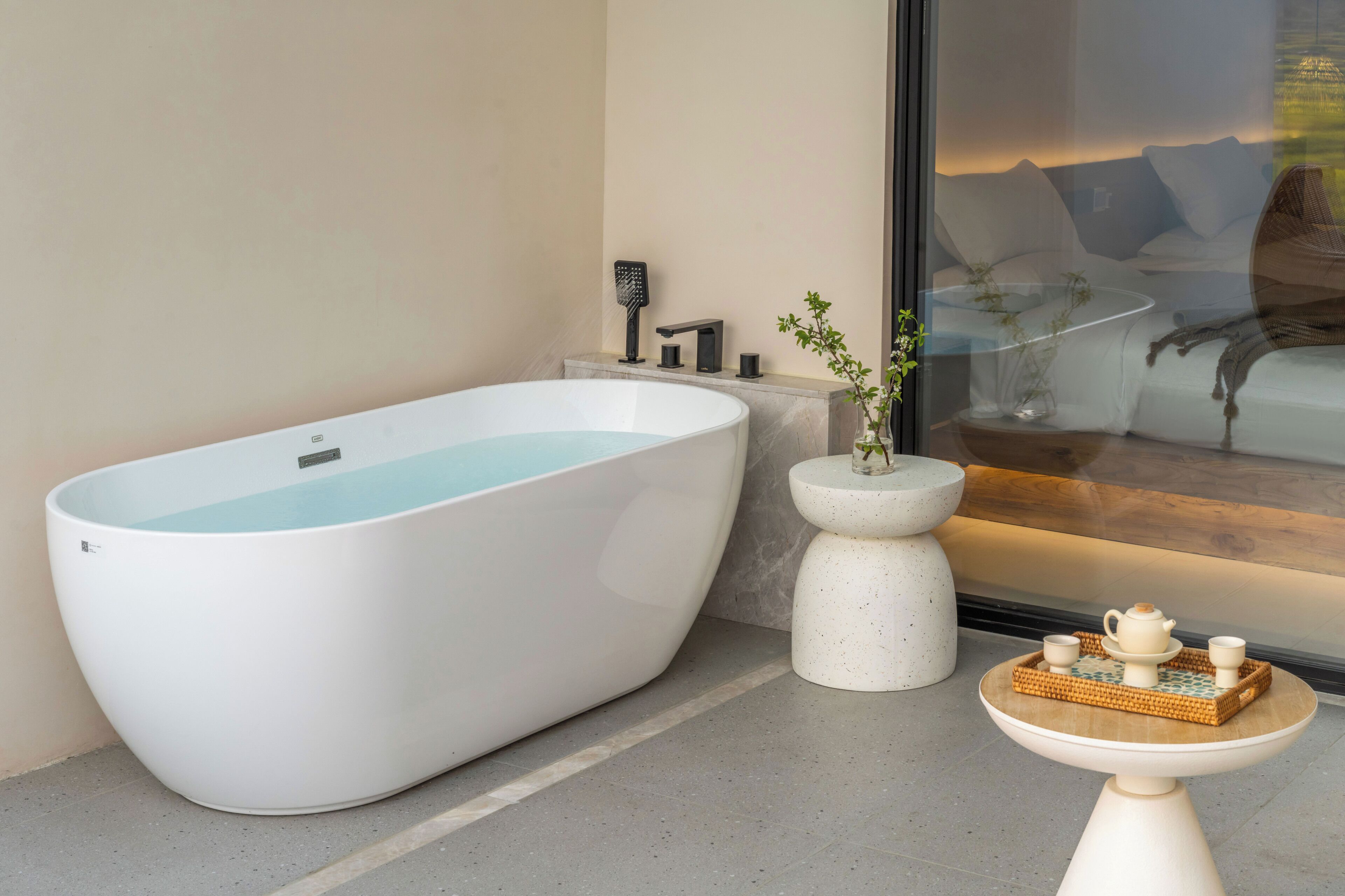 Un baño moderno con una bañera independiente, un pequeño pedestal blanco y una mesa con tetera y taza.