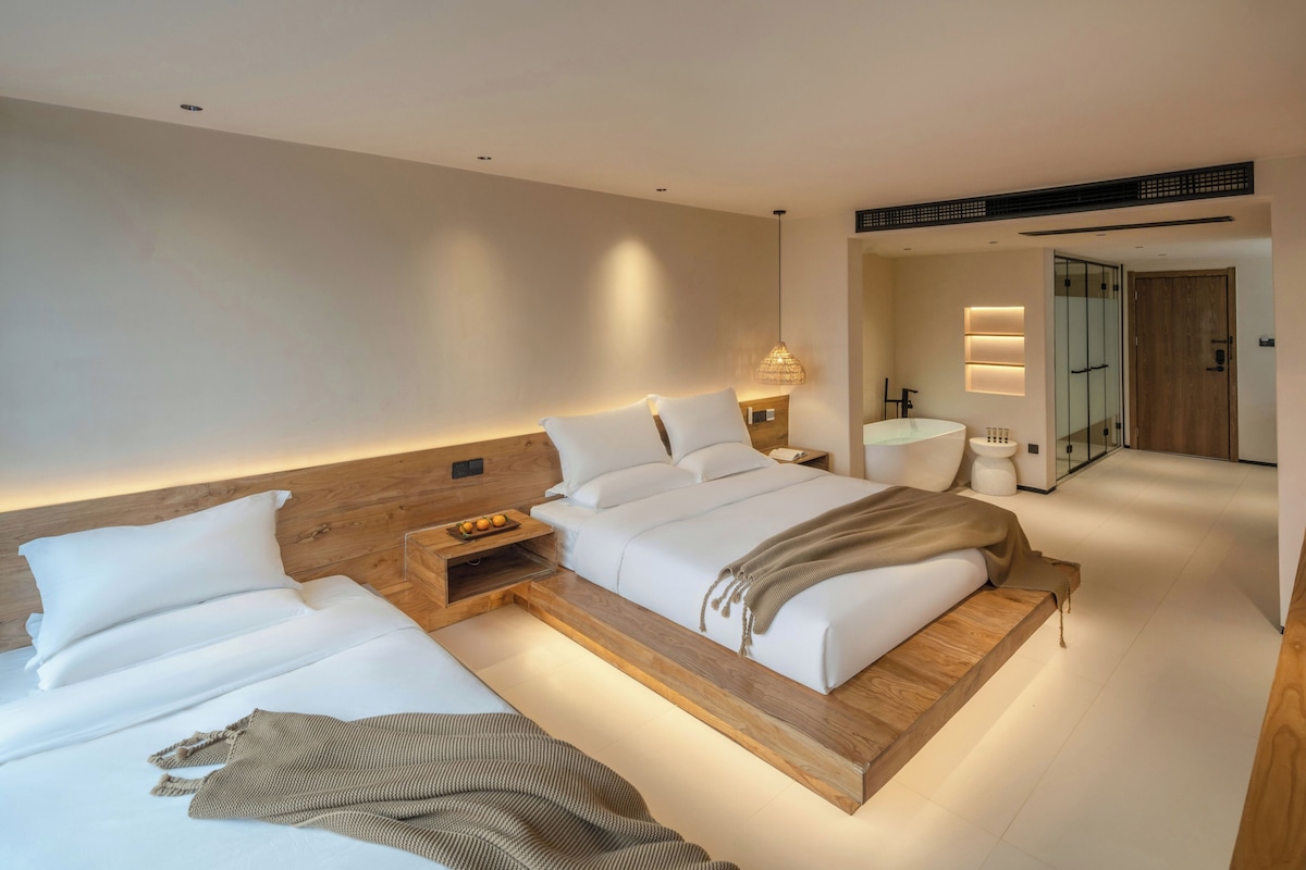 Una habitación de hotel moderna con una cama grande, mesitas de noche, una lámpara de noche, un baño pequeño y una puerta de cristal que da a la zona de la ducha.