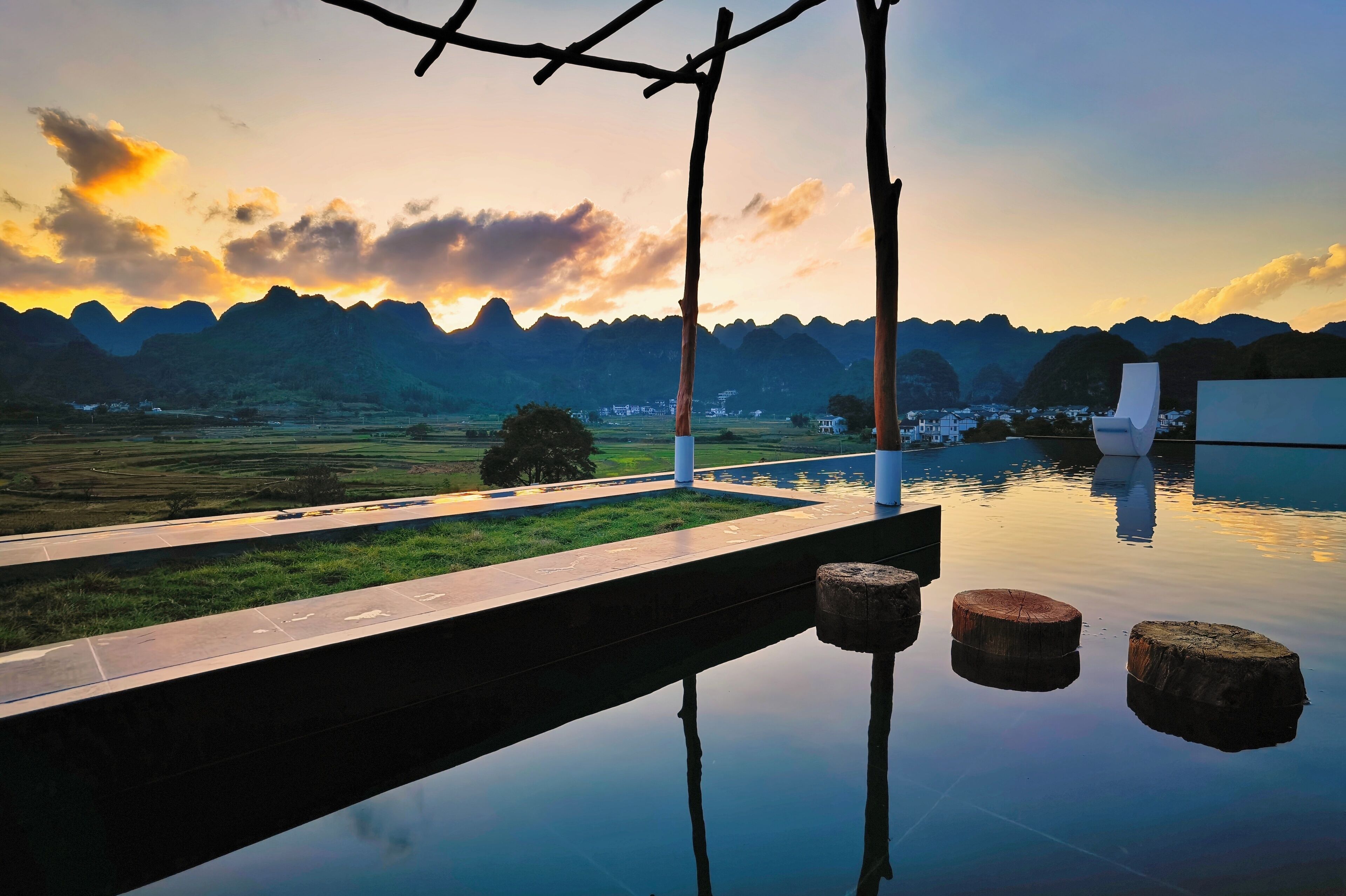 A tranquil outdoor setting with a reflective pool, a wooden deck, and a view of distant mountains.