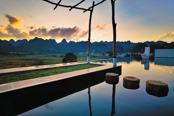A tranquil outdoor setting with a reflective pool, a wooden deck, and a view of distant mountains.