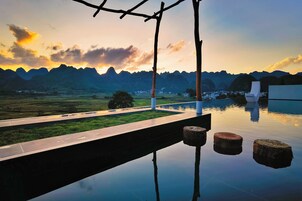 Un entorno exterior tranquilo con un estanque reflectante, una terraza de madera y vistas a montañas distantes.