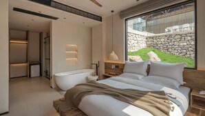 Un dormitorio moderno con una cama grande, una bañera y vistas a una pared de piedra y vegetación.