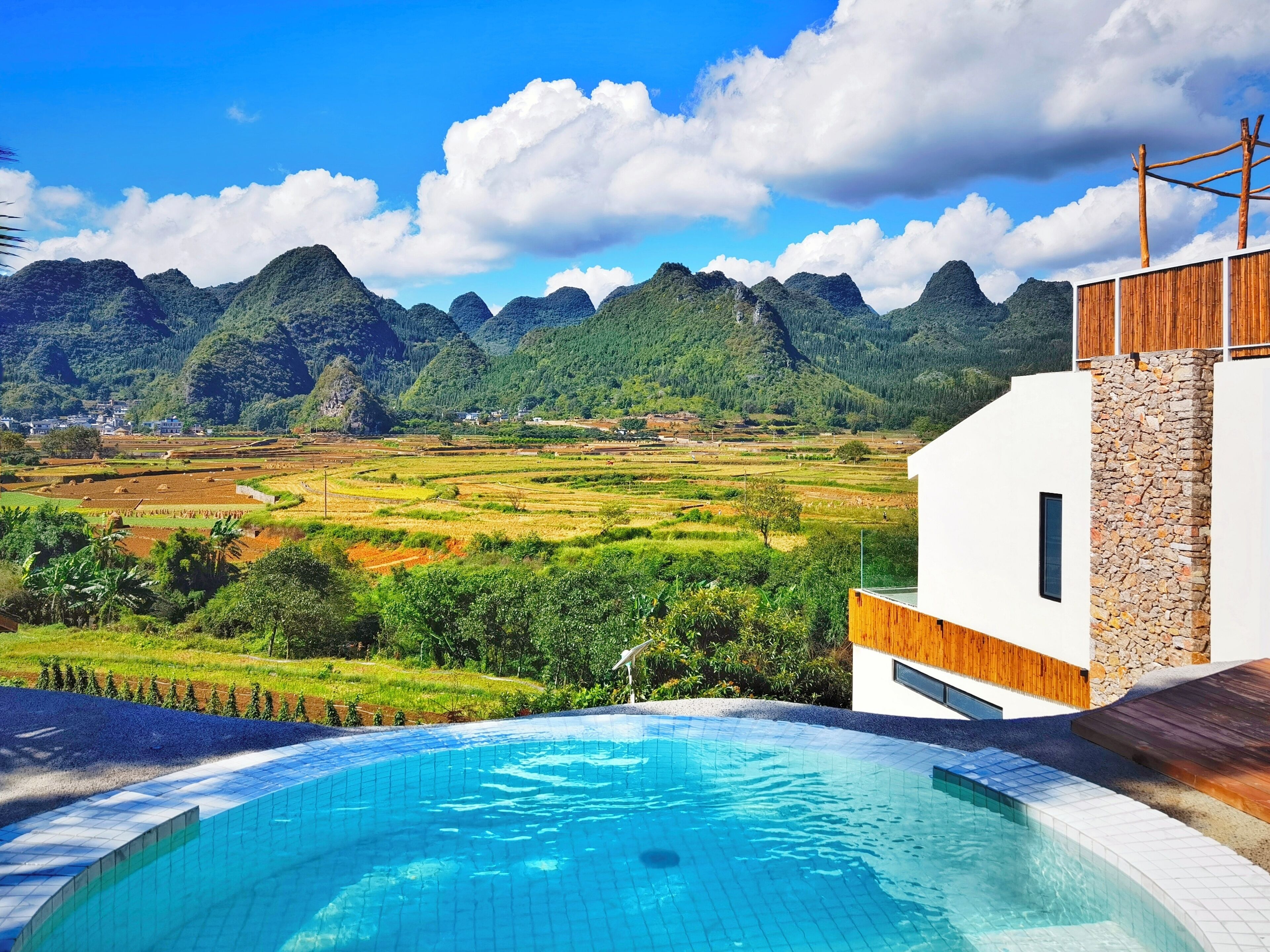 A modern building with a swimming pool, surrounded by terraced fields and mountains.