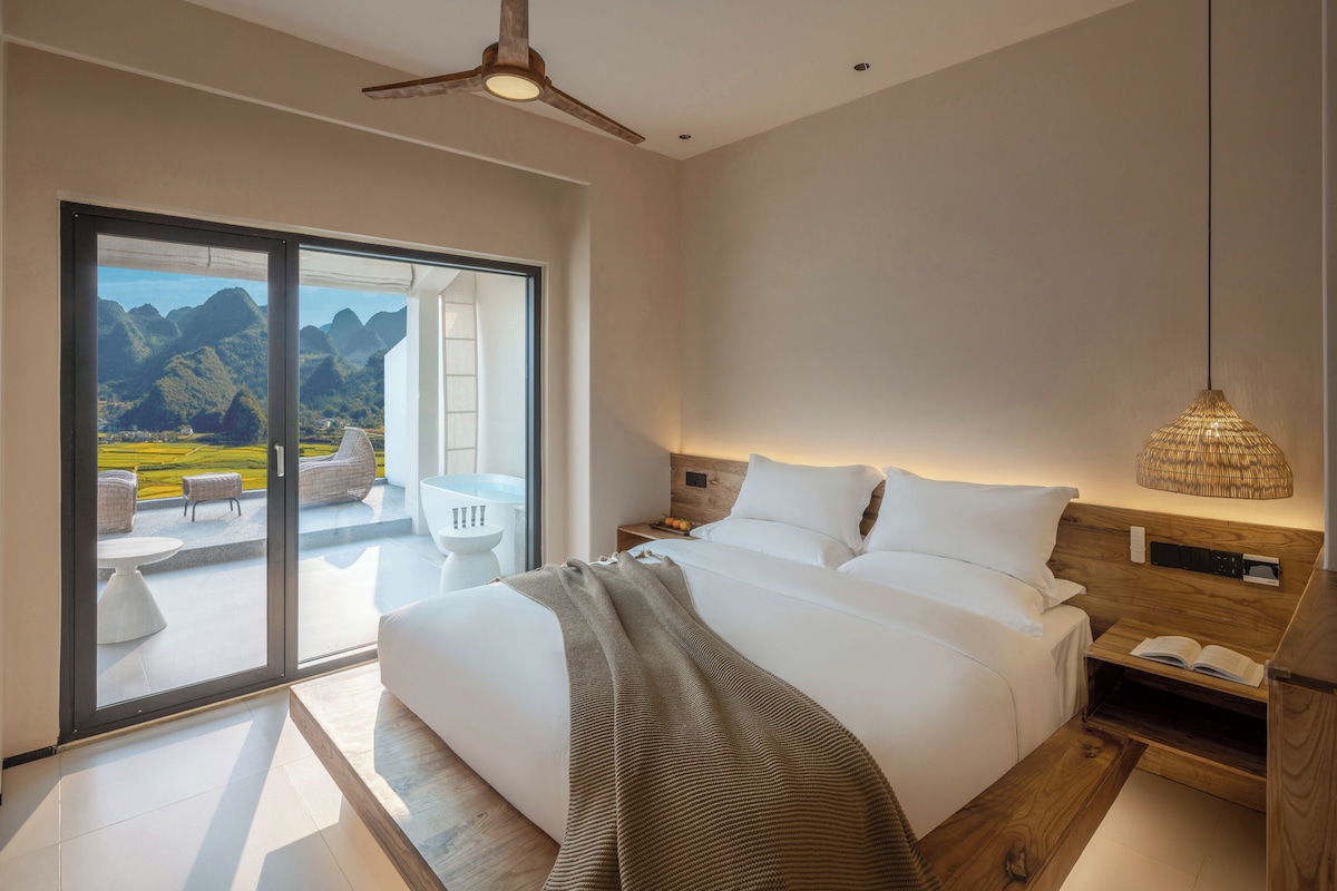 Un dormitorio moderno con una cama grande, vistas a montañas a través de una puerta corredera y un ventilador de techo.