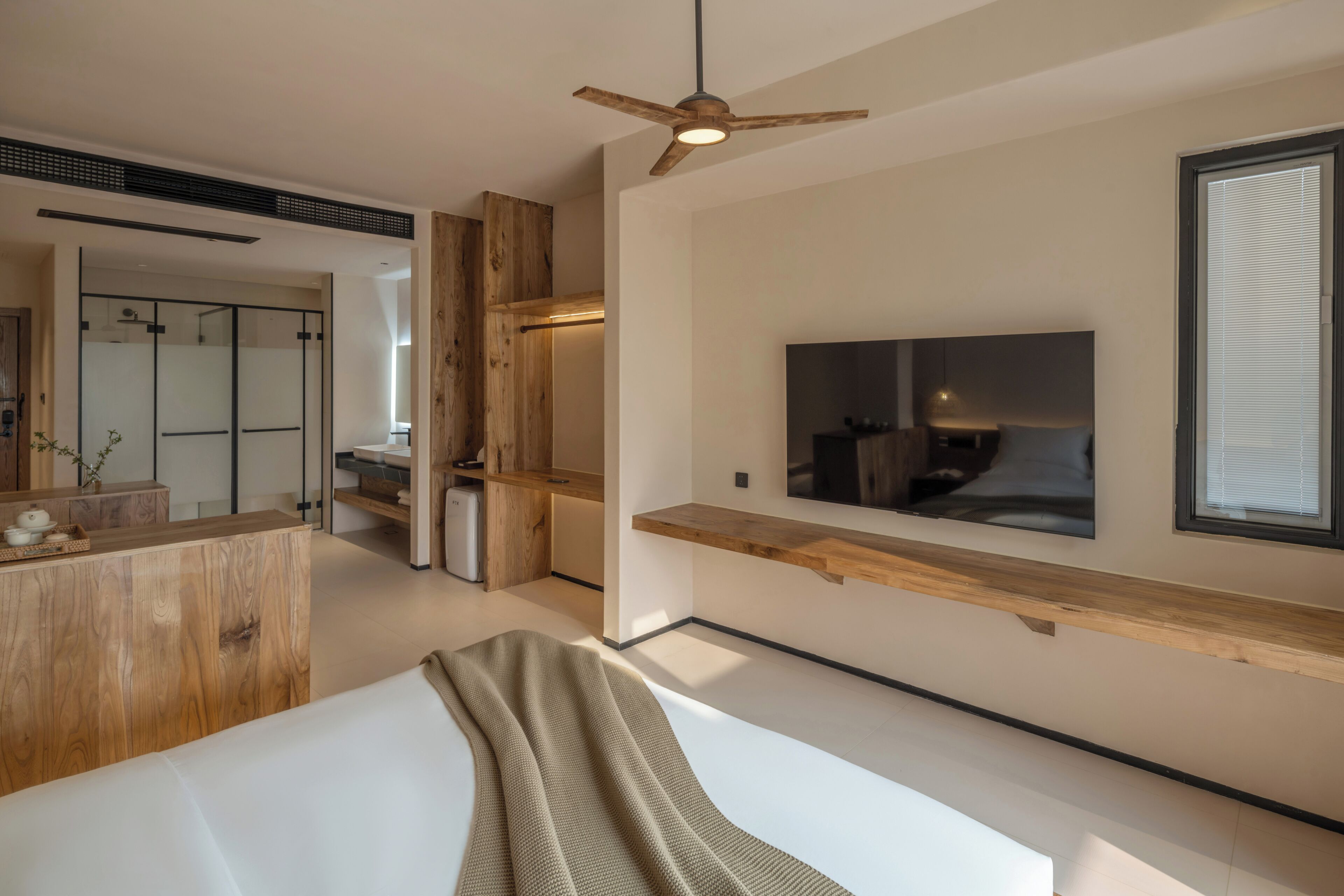 Ein modernes Schlafzimmer mit einem Bett, einem an der Wand befestigten Fernseher und einem Deckenventilator.
