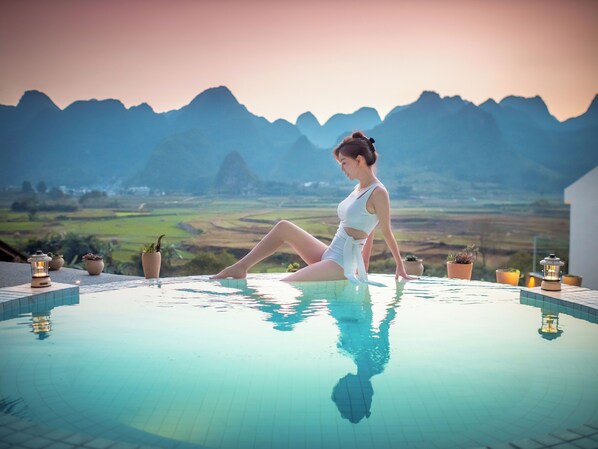 A person sitting by a pool with a mountainous landscape in the background.