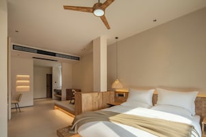 Un dormitorio moderno con cabecera de madera, cama grande con ropa blanca, lámpara colgante y ventilador de techo.
