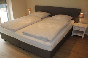 Een tweepersoonsbed met een donkere hoofdbord, twee nachtkastjes met lampen en een houten vloer.