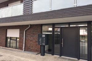 A building entrance with a black door, a mailbox, and a window with a closed shutter. - Holiday apartment with 1 bedroom (Grömitz)
