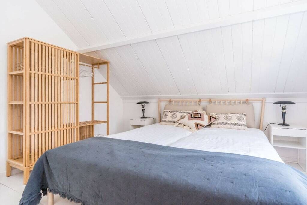 Ein Schlafzimmer mit schrägem Dach, einem Bett mit weißer Bettwäsche, einem Holzschrank und zwei Nachttischen mit Lampen.