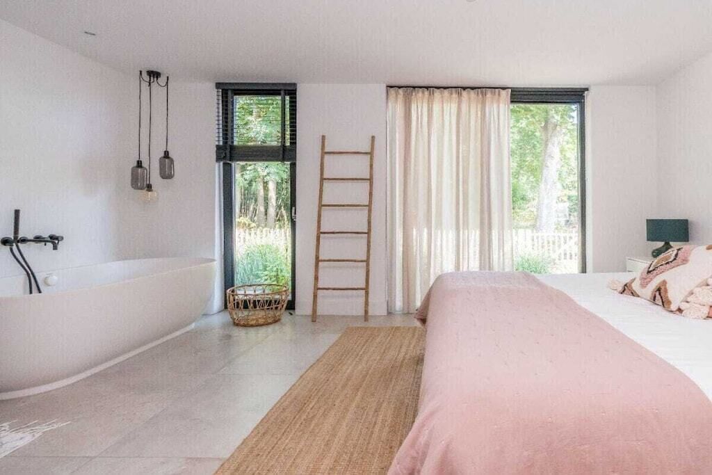 Une chambre à coucher avec un grand lit, une baignoire, une fenêtre avec des rideaux et une échelle.