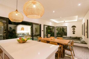 Ein modernes Interieur mit Essbereich, einer Küche mit Aussicht und einer Wohnfläche mit Sofa und Kissen.