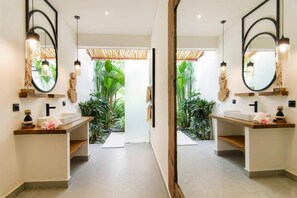 Ein modernes Badezimmer mit zwei Waschbecken, großen Spiegeln und Blick auf einen tropischen Garten.
